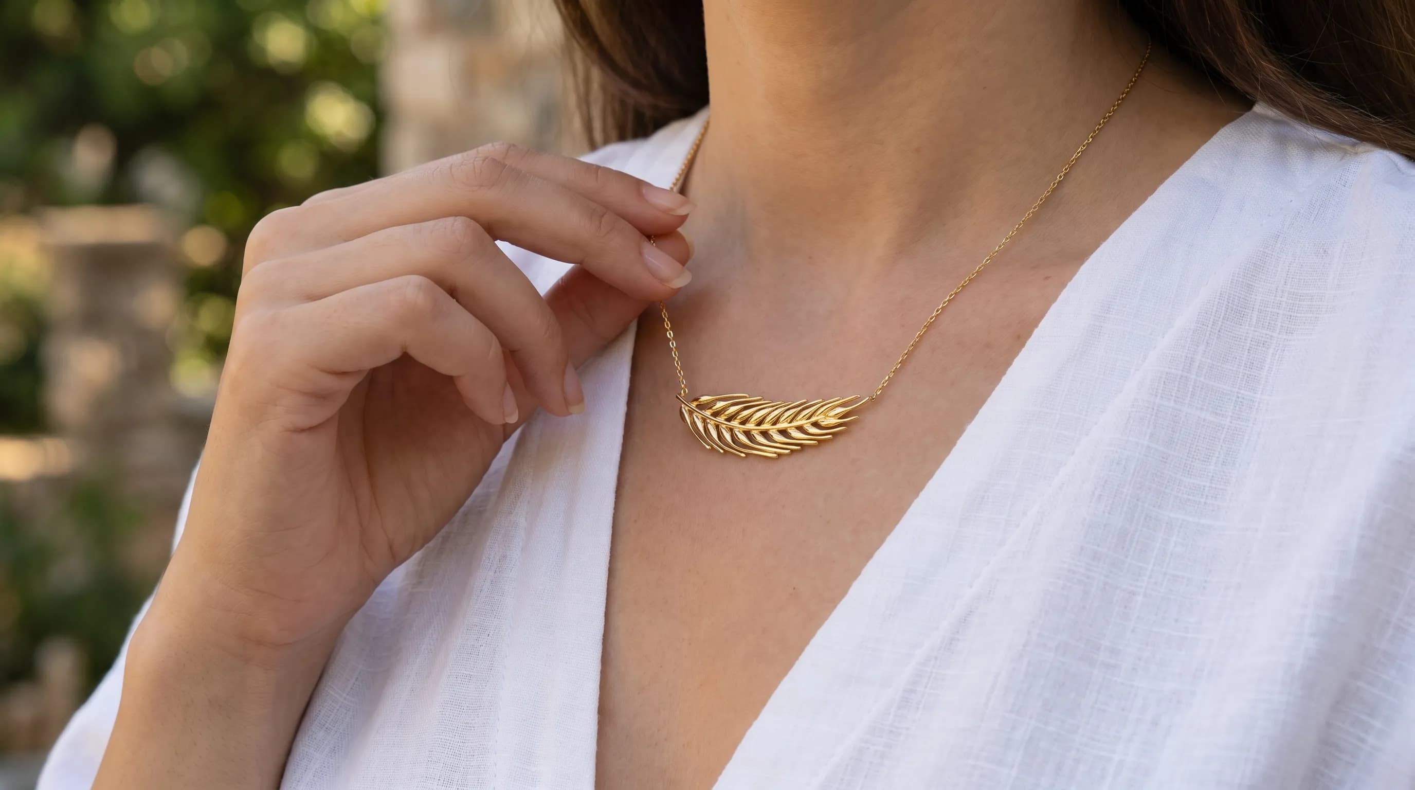 A gold wheat-shaped necklace worn outdoors, framed mid-close